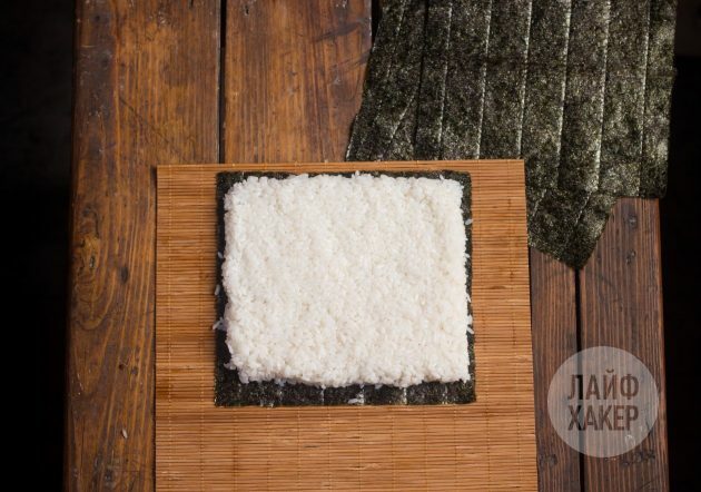 सुशीरिटो कैसे बनाएं: एक नोटी शीट को गलीचे पर रखें और इसे चावल की एक परत के साथ कवर करें